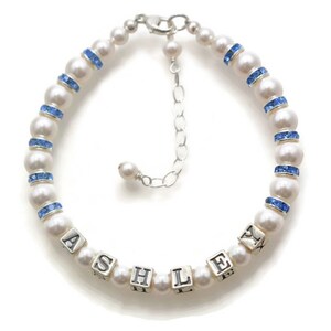 May include: A white pearl bracelet with blue crystal accents and a silver charm with the name "ASHLEY" spelled out.