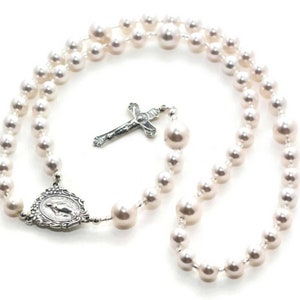 White pearl prayer beads on white background. Pearls are spaced by silver lined clear seed beads. It has a sterling silver Virgin Mary Rosary Center charm and Sterling Silver Crucifix pendant.
