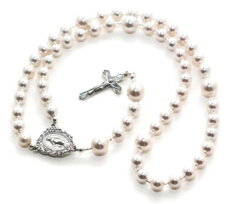 White pearl prayer beads on white background. Pearls are spaced by silver lined clear seed beads. It has a sterling silver Virgin Mary Rosary Center charm and Sterling Silver Crucifix pendant.