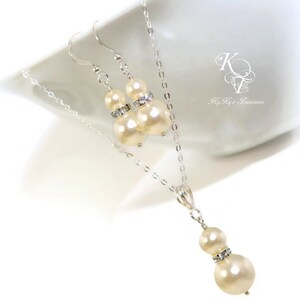 May include: A set of ivory pearl earrings and a necklace with a silver chain and a pendant featuring two ivory pearls with a crystal accent.