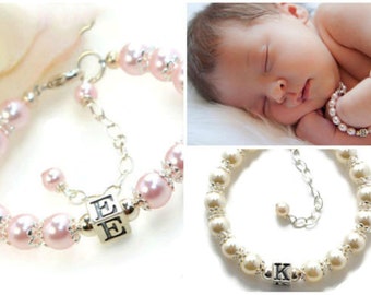 May include: Two pearl bracelets with silver charms. One bracelet has pink pearls and a charm with the letter "E" on it. The other bracelet has white pearls and a charm with the letter "K" on it.