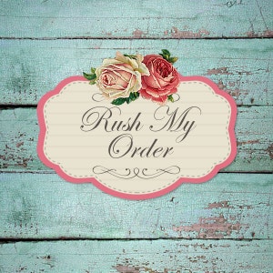 May include: A decorative sign with the text "Rush My Order" in elegant script. The sign has a pink and cream-coloured frame with a floral arrangement of pink and cream roses. The background is a distressed, turquoise-coloured wooden surface.