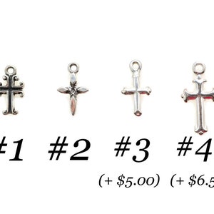 May include: Four silver-colored cross charms, each with a different design, are displayed against a white background. The crosses are labeled #1, #2, #3, and #4. The image includes text below the crosses.