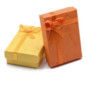 May include: Two rectangular gift boxes with textured surfaces, one in bright yellow and one in orange. Each box features a matching satin ribbon wrapped around the lid, tied into a decorative bow with a small fabric flower centered on top.