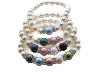 May include: A set of four stretch bracelets made of white faux pearls. Each bracelet features a central focal point consisting of colorful, iridescent beads in shades of blue, pink, green, and brown, accented by small silver-toned rhinestone spacers.