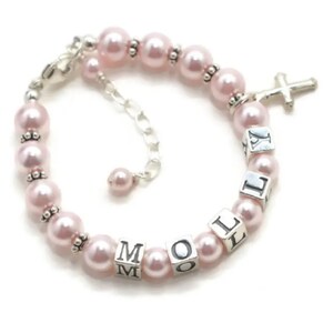 May include: A pink pearl bracelet with silver accents and a cross charm. The bracelet features the name "Mollie" spelled out with silver letter beads. The bracelet is adjustable.
