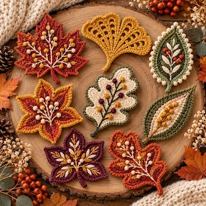 May include: A collection of eight crocheted leaves in various shapes and colors, including red, orange, yellow, green, and purple. Each leaf features intricate embroidered vein details with small bead-like accents throughout.
