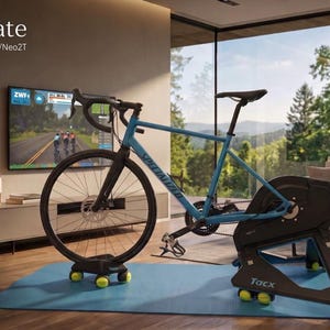 Könnte beinhalten: Ein blaues Fahrrad auf einem schwarzen Tacx-Rollentrainer mit einer Rocker-Plate, die gelbe Tennisbälle als Füße nutzt. Der Text lautet Rocker plate und Tennisballfüße für Tacx Neo/Neo2T. Das System steht auf einer blauen Matte.