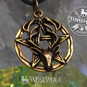 May include: A gold-toned pendant necklace featuring a five-pointed star with a deer head inside. The star is surrounded by a circle with a leafy design. The pendant is on a black cord and is resting on a green and yellow crystal.