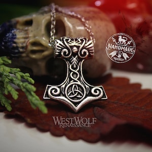 Könnte beinhalten: Silberne Mjolnir-Halskette mit filigranen Details, darunter ein keltischer Knoten und ein dreifaches Spiralmuster. Der Anhänger hängt an einer silbernen Kette und liegt auf einem braunen Blatt. Der Text "Westwolf Renaissance" ist unterhalb des Anhängers sichtbar.