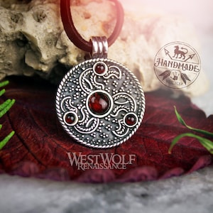 May include: Silver pendant with a circular design featuring intricate floral patterns and four red gemstones. The pendant is on a black leather cord. The text "Handmade" is visible in the background.