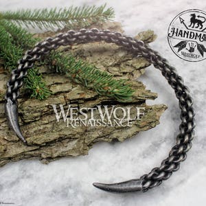 May include: A silver metal necklace with a chain design and two pointed ends. The necklace is handmade and has the text "Handmade Westwolf Renaissance" on a tag.