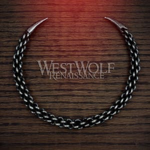 May include: A silver chain necklace with two pointed ends, forming a circle. The chain is made of linked rings, creating a textured look. The necklace is on a dark brown wooden surface.