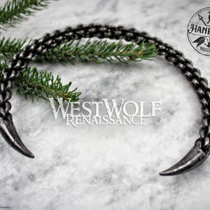May include: A silver metal choker necklace with two pointed ends. The necklace is made of a braided chain design. The necklace is handmade and is called "Westwolf Renaissance".
