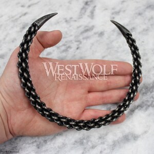May include: A silver metal necklace with a chain link design and pointed ends. The necklace is worn on a person's hand.