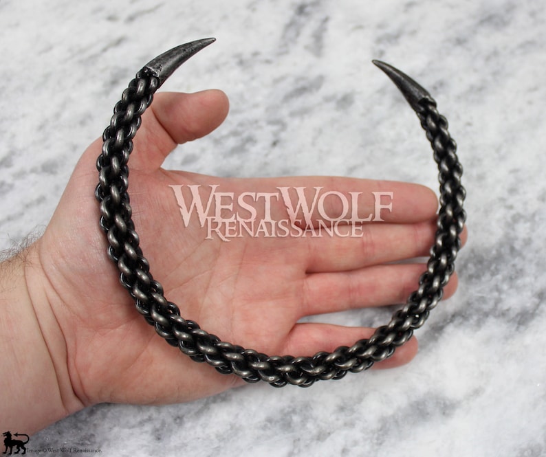 May include: A silver metal necklace with a chain link design and pointed ends. The necklace is worn on a person's hand.