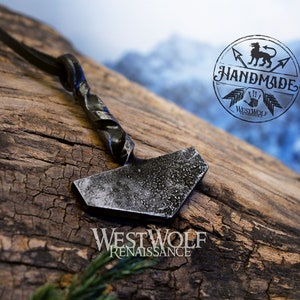 May include: A silver-colored metal hammer pendant with a twisted handle, hanging from a black leather cord. The pendant is on a wooden surface with the text "WESTWOLF RENAISSANCE" below it. A circular logo with the text "HANDMADE" and a wolf design is visible in the background.