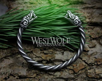 May include: A silver-toned twisted bangle bracelet with wolf head ends. The bracelet is on a green background.