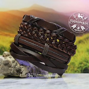 May include: A stack of brown leather bracelets with a braided design. The bracelets are stacked on a rock with a green grassy background. The text "Handmade Westwolf Renaissance" is visible in the image.
