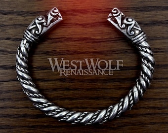 May include: A silver bracelet with a twisted rope design and dragon head ends. The bracelet is on a wooden surface.
