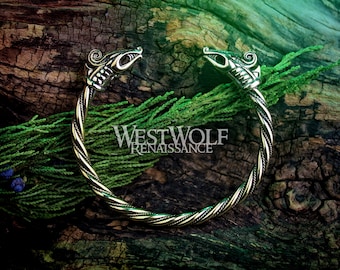 May include: A silver-toned bracelet with two dragon head ends. The bracelet is twisted and has a braided design. The bracelet is photographed on a wooden surface with green foliage.