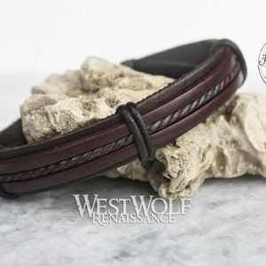 May include: A brown leather bracelet with a black braided leather design. The bracelet is handmade and has the text "Handmade Westwolf" on a tag.