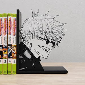 May include: A black metal bookend featuring a laser-cut silhouette of an anime character with spiky hair and round sunglasses. The bookend is positioned next to a row of five Naruto manga volumes and three One Piece manga volumes.