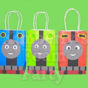 May include: Three blue, green, and red paper gift bags with Thomas the Tank Engine faces on them. The bags have white handles and are ready for party favors.