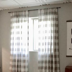 Puede incluir: Un par de cortinas de vichy blancas y marrones cuelgan en una ventana. Las cortinas son transparentes y dejan pasar la luz. Las cortinas est&aacute;n colgadas de una barra de cortina negra.