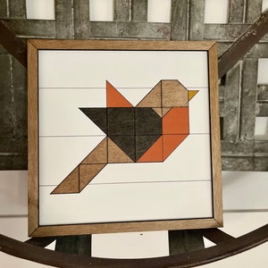 May include: A framed geometric art print of a bird with brown, black, and orange geometric shapes on a white background. barn quilt, handmade