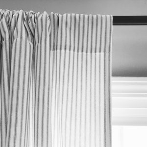 May include: A white curtain with thin black stripes hangs from a black curtain rod. The curtain is gathered at the top and the fabric is slightly wrinkled.