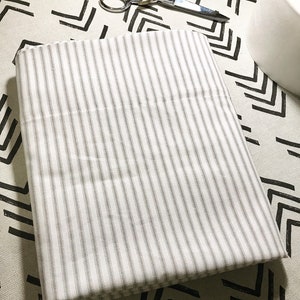 May include: A white fabric with thin gray stripes folded on a patterned surface.