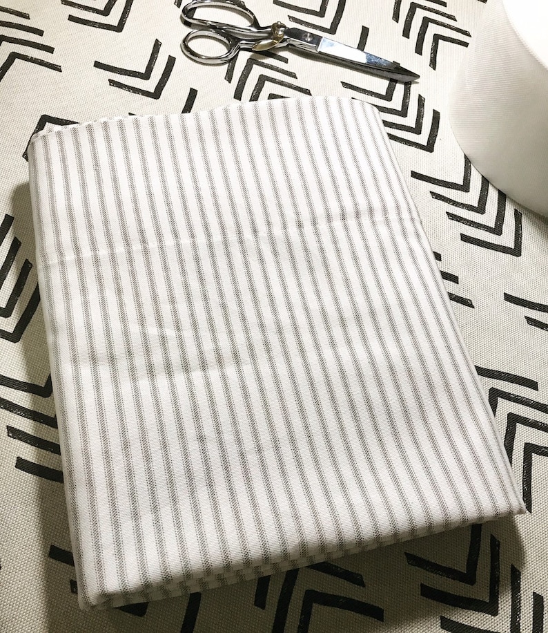 May include: A white fabric with thin gray stripes folded on a patterned surface.