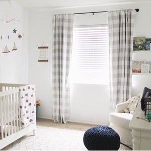 Puede incluir: Una cuna blanca con una manta de estampado marr&oacute;n y blanco, un sill&oacute;n blanco con un coj&iacute;n blanco, una cortina a cuadros azul y blanco, una l&aacute;mpara blanca con una pantalla blanca y una estanter&iacute;a blanca con libros.