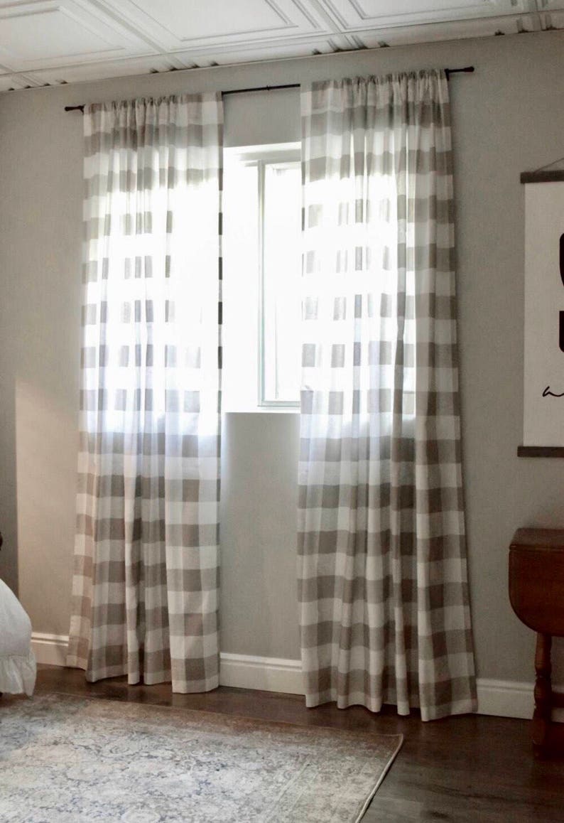Puede incluir: Un par de cortinas de vichy blancas y marrones cuelgan en una ventana. Las cortinas son transparentes y dejan pasar la luz. Las cortinas est&aacute;n colgadas de una barra de cortina negra.