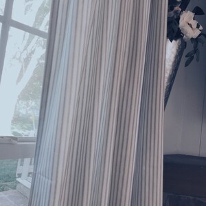 May include: A white and gray striped curtain with a white flower in a silver vase peeking out from behind it.