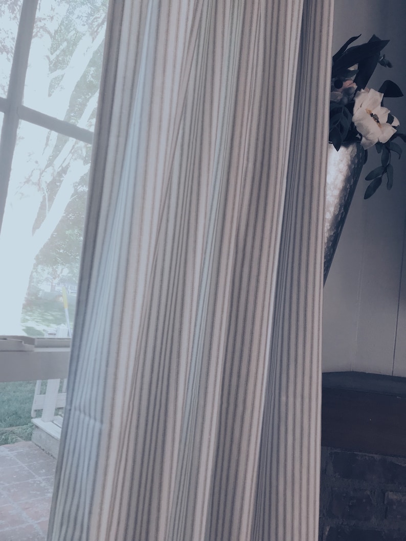 May include: A white and gray striped curtain with a white flower in a silver vase peeking out from behind it.
