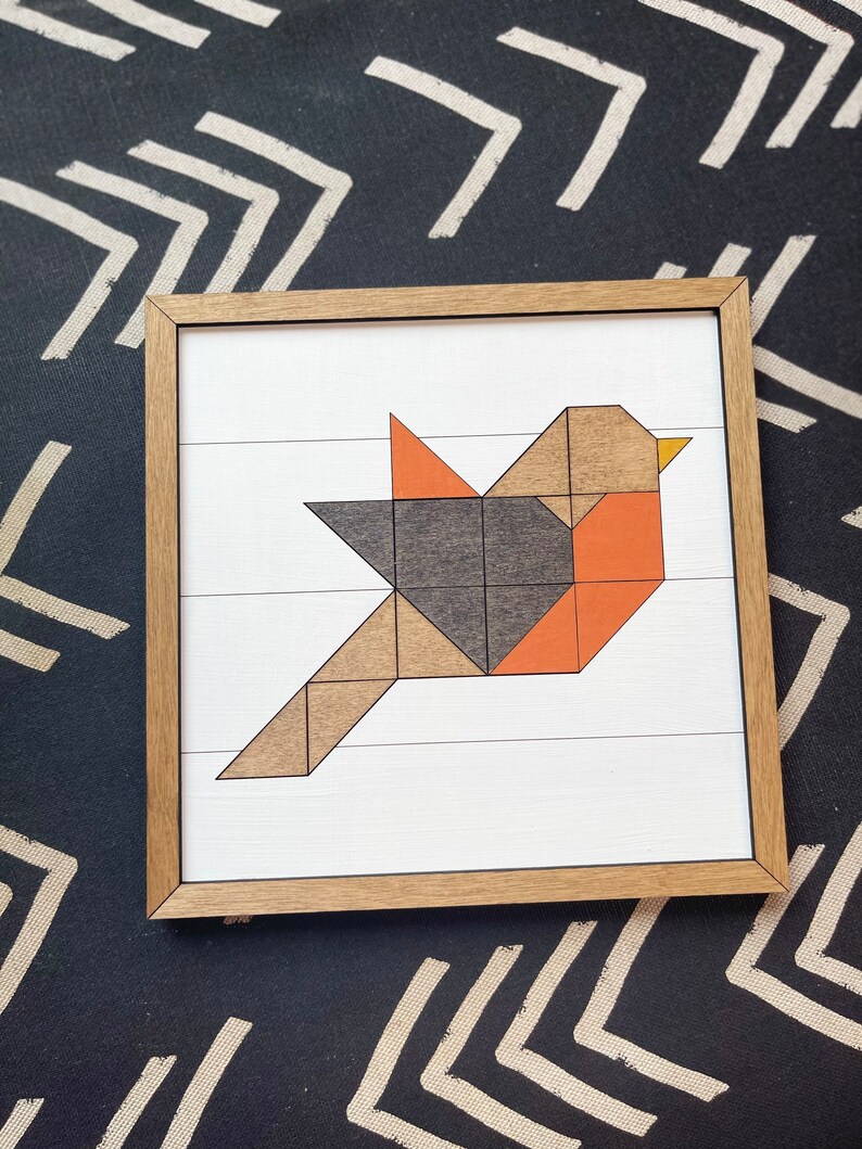May include: A framed geometric art print of a bird made from wood shapes in shades of brown, orange, and gray. The bird is flying with its wings spread out.
