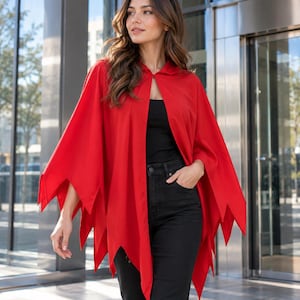 Puede incluir: Una capa de color rojo brillante con un dobladillo dentado y puntiagudo, junto con un cierre frontal sencillo, acompañada de una diadema negra adornada con dos cuernos de diablo rojos curvados. La capa se lleva sobre una camiseta negra y vaqueros.