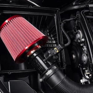 Könnte beinhalten: Ein konischer roter Luftfilter mit einer metallisch roten Basis, der an einem schwarzen Ansaugrohr mit dem geprägten Text OPEL befestigt ist. Die Baugruppe befindet sich in einem schwarzen Kunststoffgehäuse innerhalb eines Motorraums.