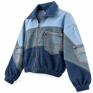 Könnte beinhalten: Eine farblich abgesetzte Jeansjacke mit hellblauem Kragen und Brustbereich, einem mittelblauen Mittelteil und einem dunkelblauen Unterteil. Sie verfügt über einen Frontreißverschluss, elastische Bündchen am Saum und an den Ärmeln sowie zwei Taschen.