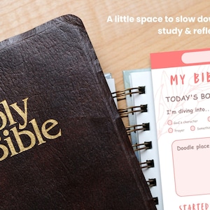Può includere: Una Sacra Bibbia rilegata in pelle marrone scuro accanto a un'agenda di studio a spirale con accenti rosa. L'agenda presenta il testo 'MY BIBLE STUDY', 'TODAY'S BOOK', 'I'm diving into...' e 'Doodle place'. Il testo sopra recita 'A little space to slow down, study & reflect.'