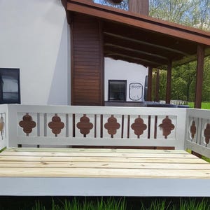 May include: White wooden bench with a decorative back featuring a repeating pattern of brown quatrefoils. The bench is outdoors and has a wooden slatted seat.