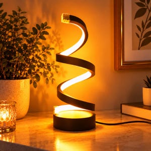 Peut inclure: Une lampe de table noire en forme de spirale avec une bande lumineuse LED continue le long de la courbe intérieure. La lampe possède une base circulaire et émet une lueur dorée et chaude, diffusant une lumière douce alentour.