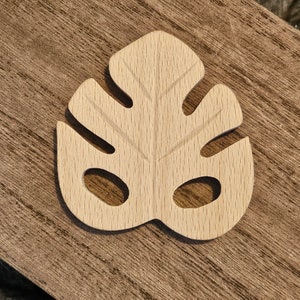 May include: A light wood carving of a monstera leaf with cutouts. The leaf is a natural wood color and has a smooth finish.