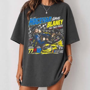 May include: A charcoal gray oversized t-shirt featuring a graphic print of race car drivers Carson Hocevar and Ryan Blaney. The text reads HOCEVAR GAVE BLANEY THE TWO-PIECE, SOME RACES HIT DIFFERENT, NASCAR AFTER DARK, and includes the numbers 77 and 12.