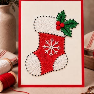 Könnte beinhalten: Ein Fadenkunst-Projekt auf einem rechteckigen Brett mit einem rot-weißen Weihnachtssocken-Motiv. Die Socke ist mit schwarzen Stiften umrandet und mit weißem sowie rotem Garn gefüllt, akzentuiert durch grüne Stechpalmenblätter und rote Beeren.