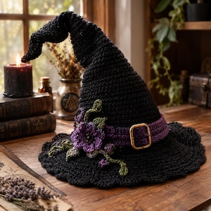 May include: A black crocheted witch hat featuring a pointed, slightly curved top and a wide brim. A purple crocheted band encircles the base, adorned with a gold-toned metal buckle and a cluster of purple crocheted flowers and green leaves.