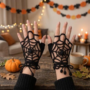 May include: A pair of black fingerless gloves featuring a crocheted spiderweb pattern with a small spider at the center of each web. The gloves have a tie closure at the wrist with dangling accents and leave the fingers and thumb exposed.