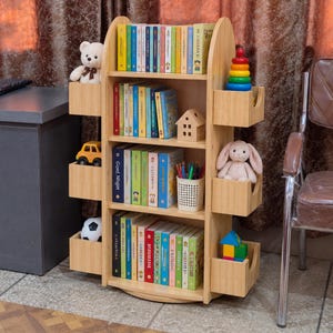 May include: A light wood rotating bookshelf with three main shelves and six side storage compartments. The shelves are filled with various books, a small wooden house, a pencil holder, and toys including a teddy bear, a rabbit, a car, a ball, and blocks.